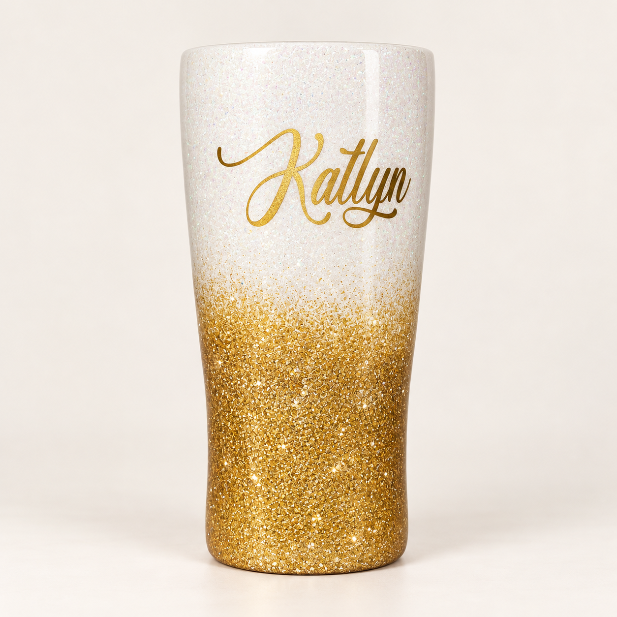 A white glitter tumbler fading into gold glitter, with the name Katlyn written in gold script lettering